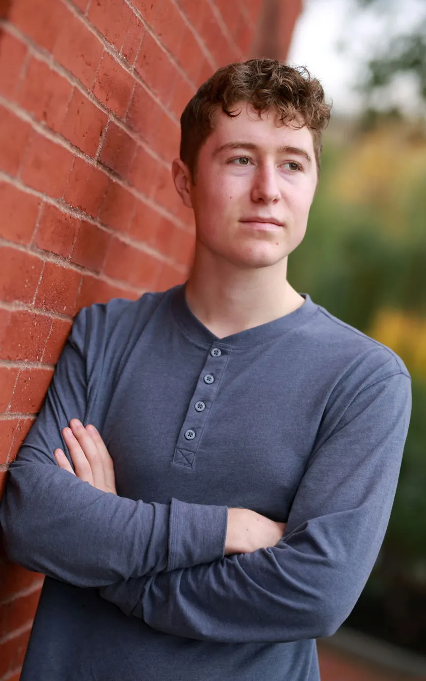 A young man leaning against a brick wall with arms crossed