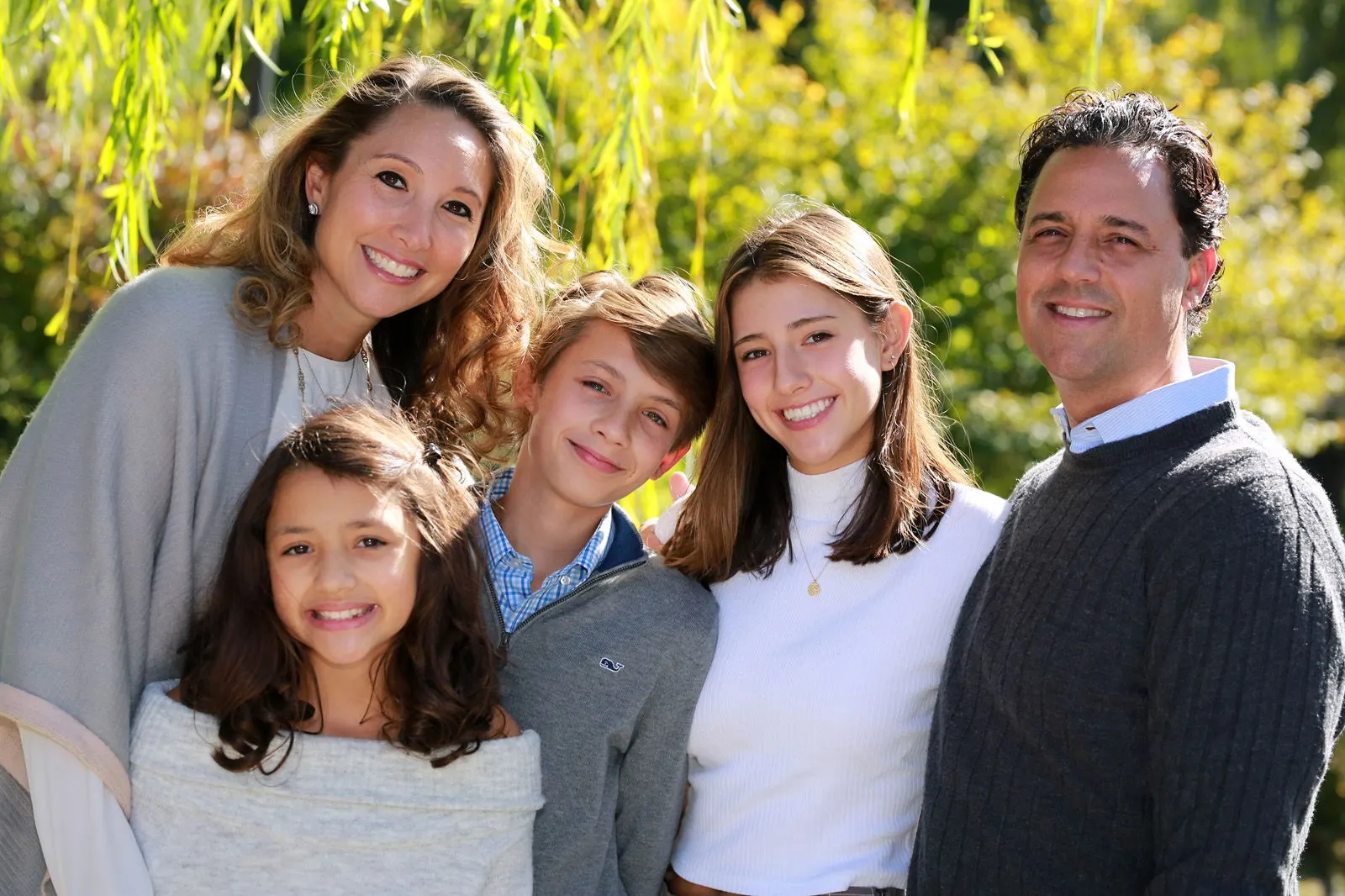A family of five smiling together under golden autumn leaves
