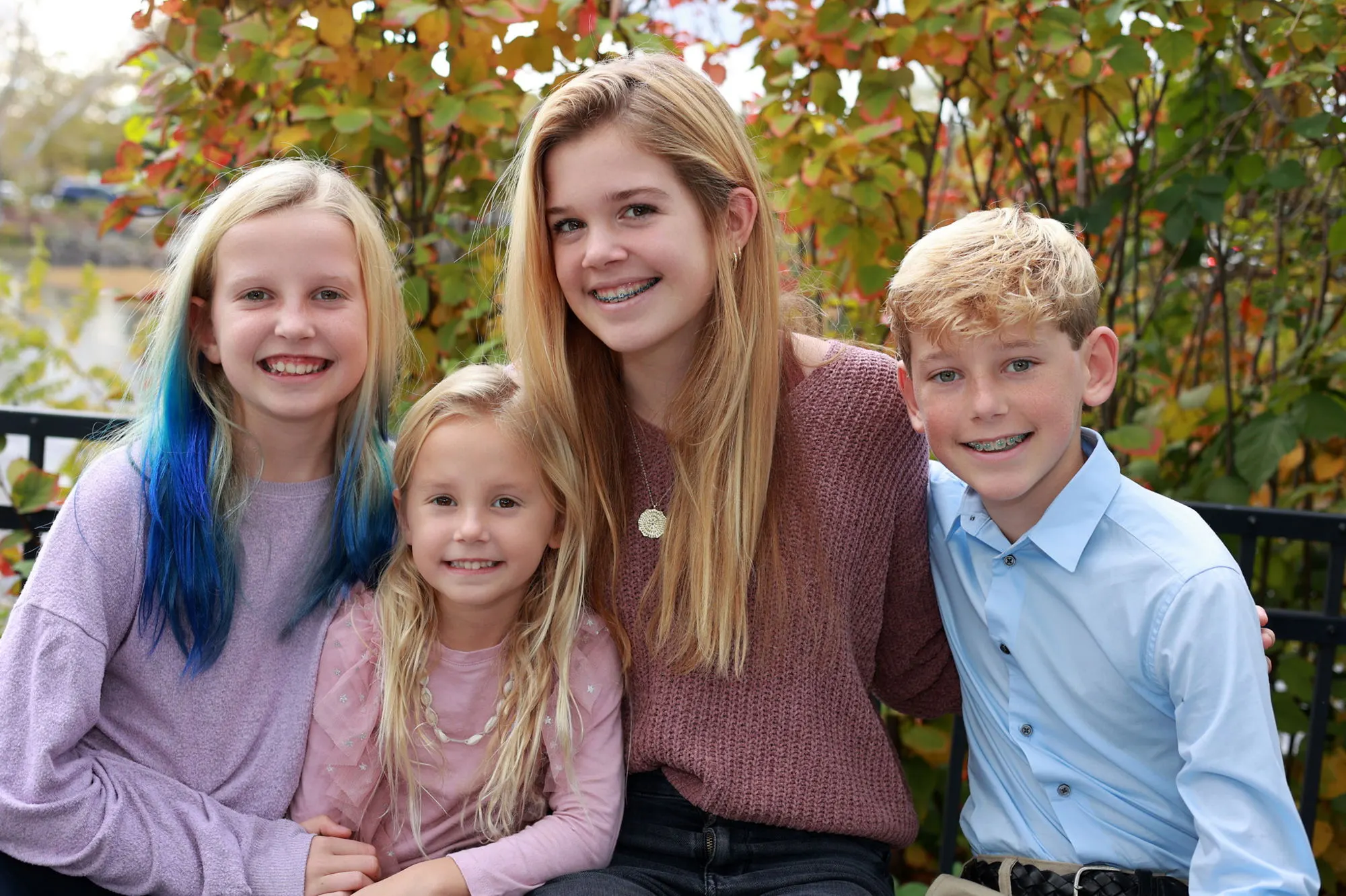 Three siblings posing together in front of fall foliage