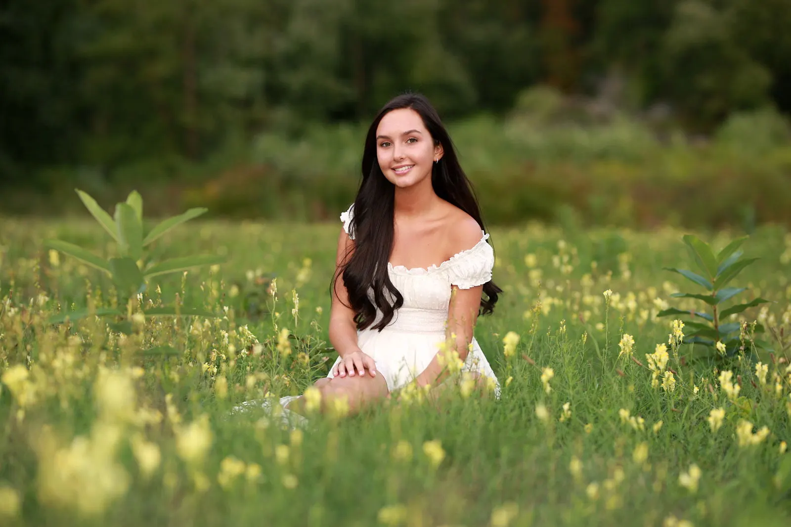 A young woman in a white dress sitting in a sunlit meadow
