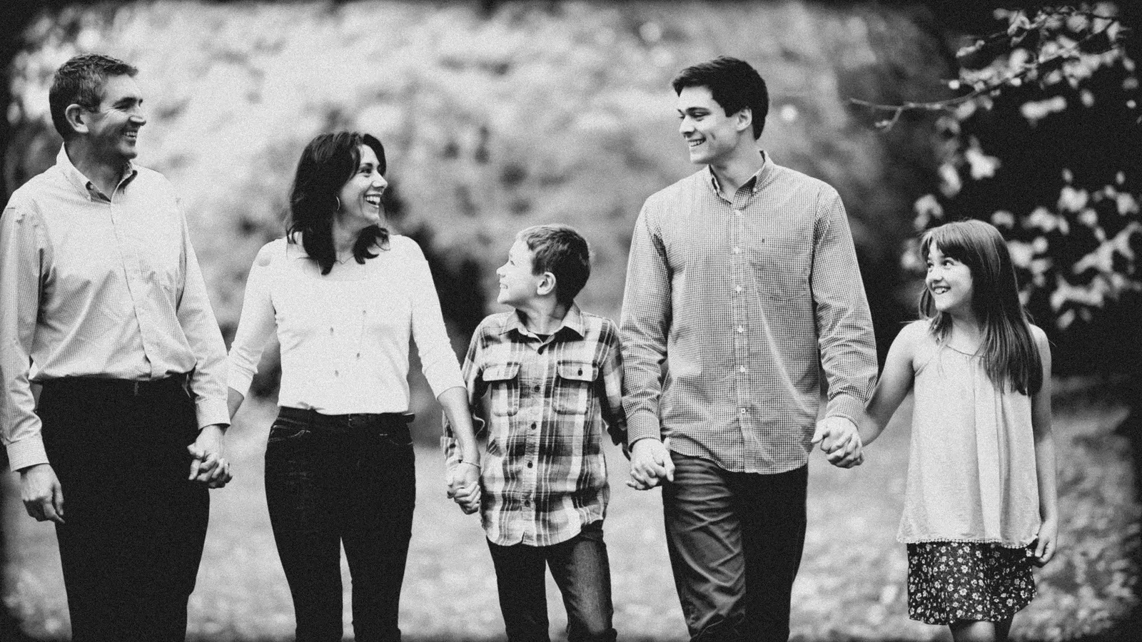 A family of five walking hand in hand, laughing, in black and white